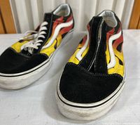 Front view of the pair of Vans shoes showing flame design on the sides, white rubber soles with dirt marks, and the zipper closure on the top.