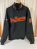 Front view of black San Francisco Giants jacket with orange script and logos.
