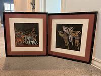Two framed Asian themed fabric wall art pieces propped on carpet, showing battle scene and horses