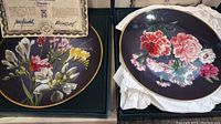 Photo of two floral collector plates in original boxes with certificates of authenticity visible.