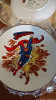 Superman collector plate front showing colorful image of Superman bursting through brick wall with red cape and 'Superman' text