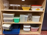 Various plastic food storage containers and serving trays of different sizes and colors arranged on wooden shelves.
