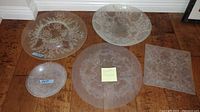 Full set of five Dorothy Thorpe etched glass serving plates on wooden floor, includes large round plates and one rectangular plate.