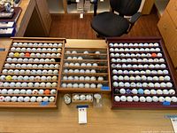 Photo of three wooden display cases on a table with various golf balls arranged inside them, two cases covered by plexiglass and one open