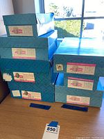 Stack of nine blue Madame Alexander original boxes labeled with doll details and collections.