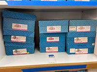 Blue and pink original boxes for Madame Alexander dolls stacked on a shelf.