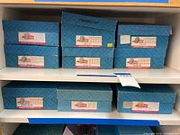 Seven blue Madame Alexander boxes on shelves, labeled and stacked in two rows.