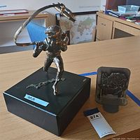 Metal schoolboy sculpture on black base with a metal bookend next to it on a wooden table.