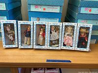 Full view of seven Shirley Temple dolls in original Ideal boxes lined up on a table.