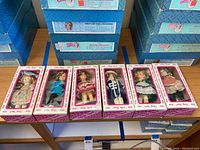 Seven Shirley Temple dolls, all in original boxes, displayed side by side on a wooden table.