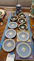 Multiple Wedgwood blue jasperware small plates, heart-shaped dish, container with lid, and a bell displayed on a table.