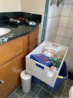 White basket filled with assorted medical and bathroom supplies placed on the floor near a bathroom cabinet and shower.