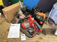Three chain saws including a Homelite with red body and manual, a Black & Decker orange battery-powered chain saw, and a Rousong electric chain saw with black and red parts.