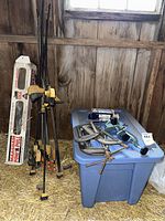 Various bar clamps leaning against wall beside boxed come-along