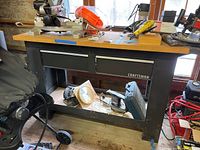 Full frontal view of Craftsman workbench showing wooden top, two metal drawers, open storage with miscellaneous items underneath.