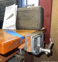 Dremel branded hard plastic carrying case with owner's manual on a wooden workbench, showing the packaging of the rotary tool.