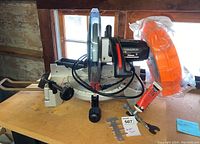 Side view of the Craftsman 10-inch compound miter saw with power motor and base, safety guard attachment, and accessories on wooden surface near a window.