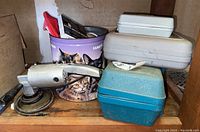 Photo of metal Makita power planer with attached dust collection bag, stored alongside Dremel case and other tool cases on wood shelf.