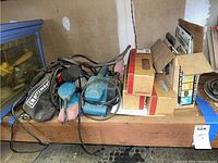 Top down view of bundled corded sanders including Craftsman and Makita with sanding belts and boxes on wood shelf.