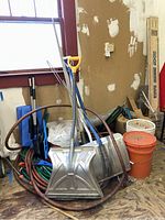 Snow shovels leaning against wall with garden hoses coiled on floor, orange and white pails present