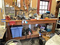 Full front view of wooden work bench with clutter on top and underneath showing construction and condition with visible scratches and wear.