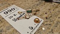 Both brooches displayed on an auction lotted tag. One is a detailed cameo in 10K gold filigree frame, the other a green stone with seed pearl bar brooch also marked 10K.