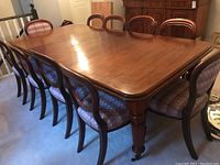 Wide view of antique cherry wood dining table with eight chairs arranged around it.