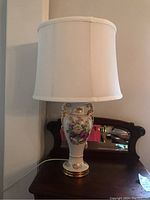 Full view of porcelain floral lamp with fabric shade on wooden table