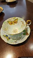 Teacup seated on saucer showing full butterfly pattern and scalloped gilt rim