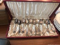 Eleven spoons displayed inside an open red Birks case with satin-lined interior