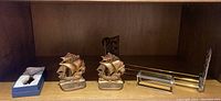 Shelf showing two brass sailing ship bookends and a magnifying reader in a blue box, along with a decorative brass magnifying glass with a detailed stand.