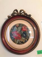 Full view of the framed needlepoint with floral design and bow accent on top of the frame.