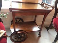Side view of antique wooden tea cart showing large wooden wheels and lower shelf