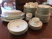 Full view of the Limoges china set displaying stacks of plates, arranged tea cups and saucers, lidded casserole dish and serving platters on table