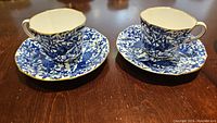 Set of two Royal Crown Derby coffee cups with matching saucers on wooden table.
