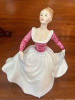 Front view of Royal Doulton porcelain figurine with pink top and white skirt on a wooden surface.