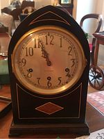 Front view of Seth Thomas mantel clock showing arched wood case, brass rimmed clock face, and inlaid wood design.