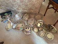 Main layout of all pieces on floor showing cocktail shaker, trays, covered dishes, bowls, coaster, cup, tongs, salt cellar and spoon