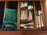 Top view of selected forks, spoons, knives and two fabric silverplate protector bags in wooden flatware organizer tray.