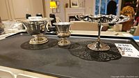 Overview of all three sterling silver pieces on black tray: pedestal dish with glass liner, egg cup, and lattice pedestal dish