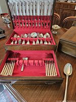 Open chest showing top tray with shell-pattern knives in lid and matching forks and spoons beneath.