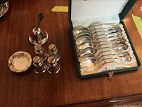 All 14 pieces displayed on wood surface: teaspoons in open case, sugar caster, four shakers, decorative dish
