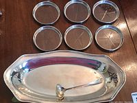 Six round coasters arranged above an elongated platter with ladle inside platter