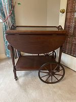 Wooden tea cart with drop leaves folded down, showing front view and wheel design