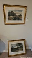 Two framed vintage landscape prints on and against a wall, gold ornate frames, depicting cattle near water and trees