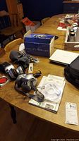 Photo of Canon PowerShot PC1130 camera, multiple lenses, manuals, CDs, and Toshiba portable DVD player arranged on wooden dining table.
