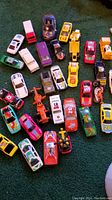 Top-down view of 31 assorted toy cars and trucks in various colors and styles on green carpet.