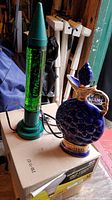 Photo showing both the green Crayon lava lamp and the Jim Beam blue commemorative bottle together on a box