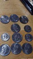 Photo showing 11 silver-tone coins arranged on a table, including Eisenhower dollars and Kennedy halves, displaying profiles of Eisenhower and Kennedy.
