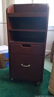 Front view of wooden file cabinet with open shelves and two drawers on wheels.